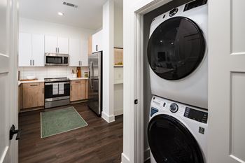 A white washing machine is in a laundry room with a green rug and a microwave above the stove.